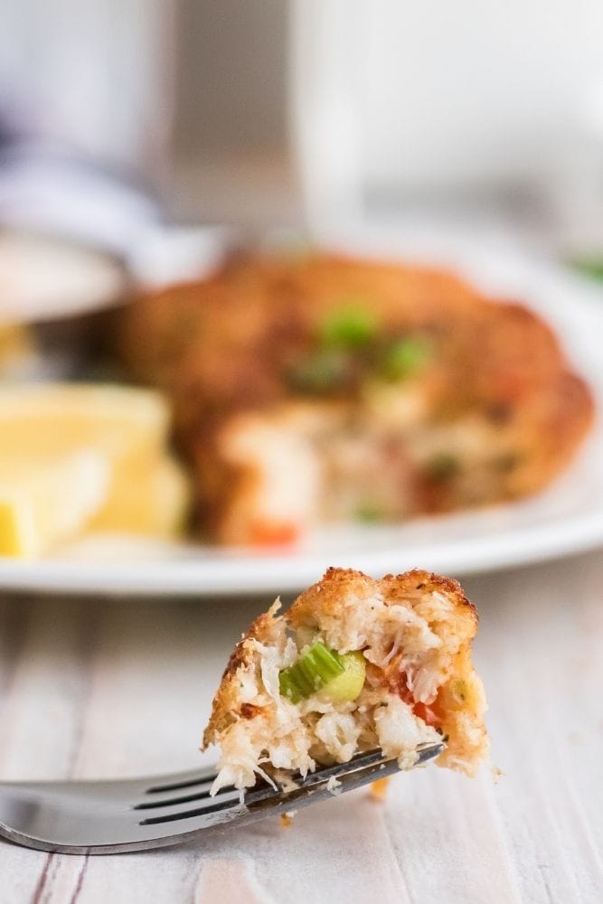 Garfo com um pedaço de bolo de caranguejo da fritadeira com prato ao fundo