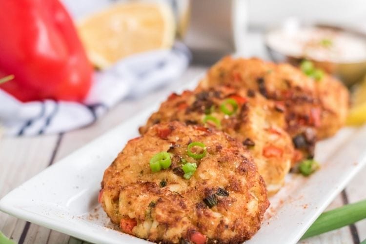 Bolos de caranguejo Air Fryer espalhados em um prato branco com guarnição verde por cima