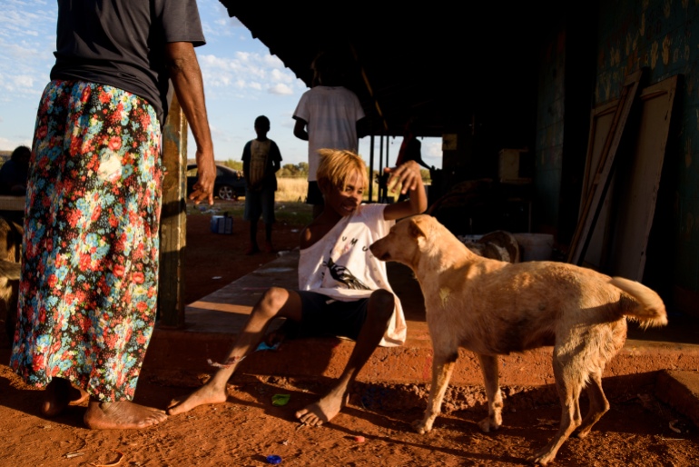 Um cachorro fica na frente de uma criança que está acariciando o animal.  Algumas pessoas estão de pé ao redor deles.
