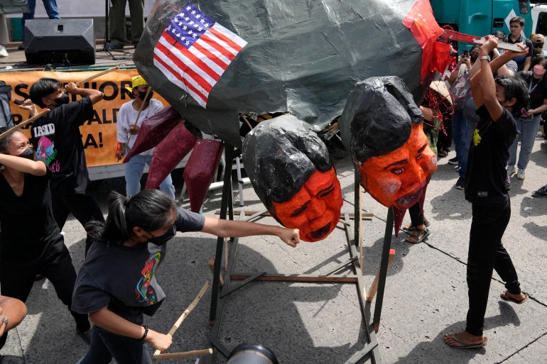 Os manifestantes socam uma efígie de Ferdinand Marcos Jr. Ela também é pintada com uma bandeira dos Estados Unidos.
