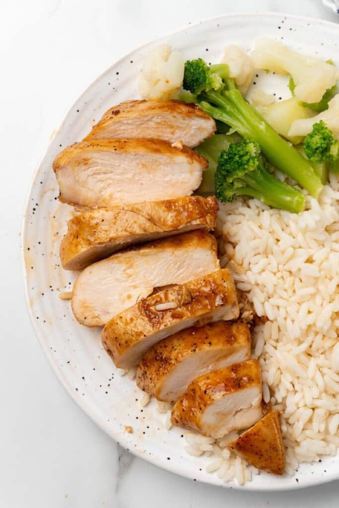 Visão aérea de fatias de peito de frango com arroz e brócolis em um prato branco.