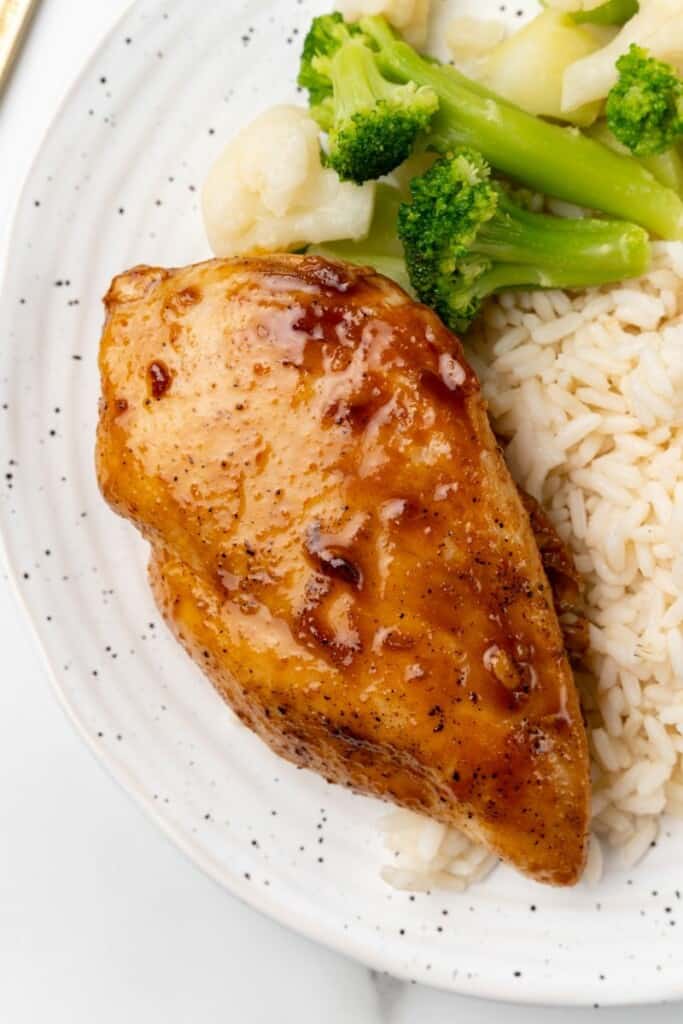 Visão aérea de um peito de frango com arroz e brócolis em um prato branco.