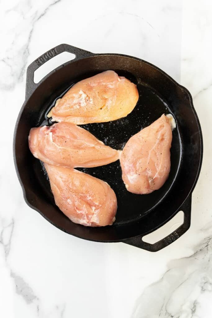 Visão aérea de peitos de frango cozinhando em uma frigideira de ferro fundido.