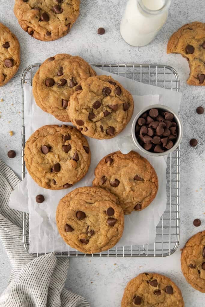 Biscoitos com gotas de chocolate deitados em uma grade de resfriamento com uma folha de papel manteiga embaixo deles.