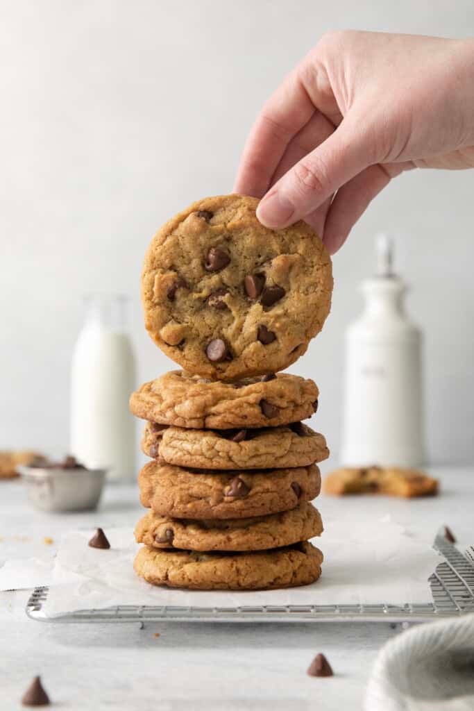 Pilha de biscoitos de chocolate assados ​​com um levantado, garrafas de leite ao fundo.