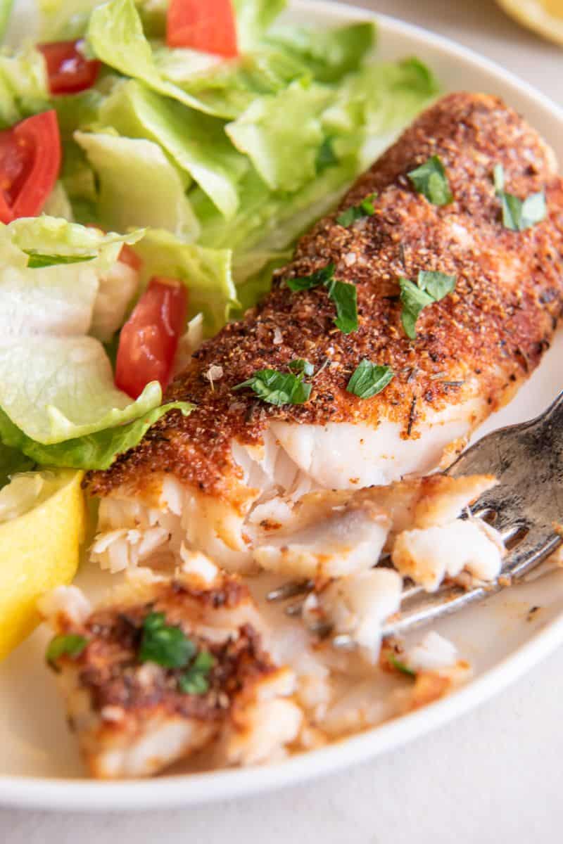 Pedaços de bacalhau frito num prato branco com uma pequena salada ao fundo.