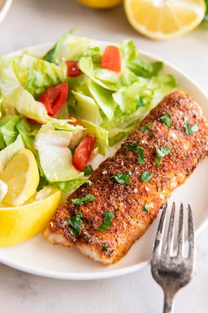 Bacalhau frito ao ar em um prato branco com salada e rodelas de limão.