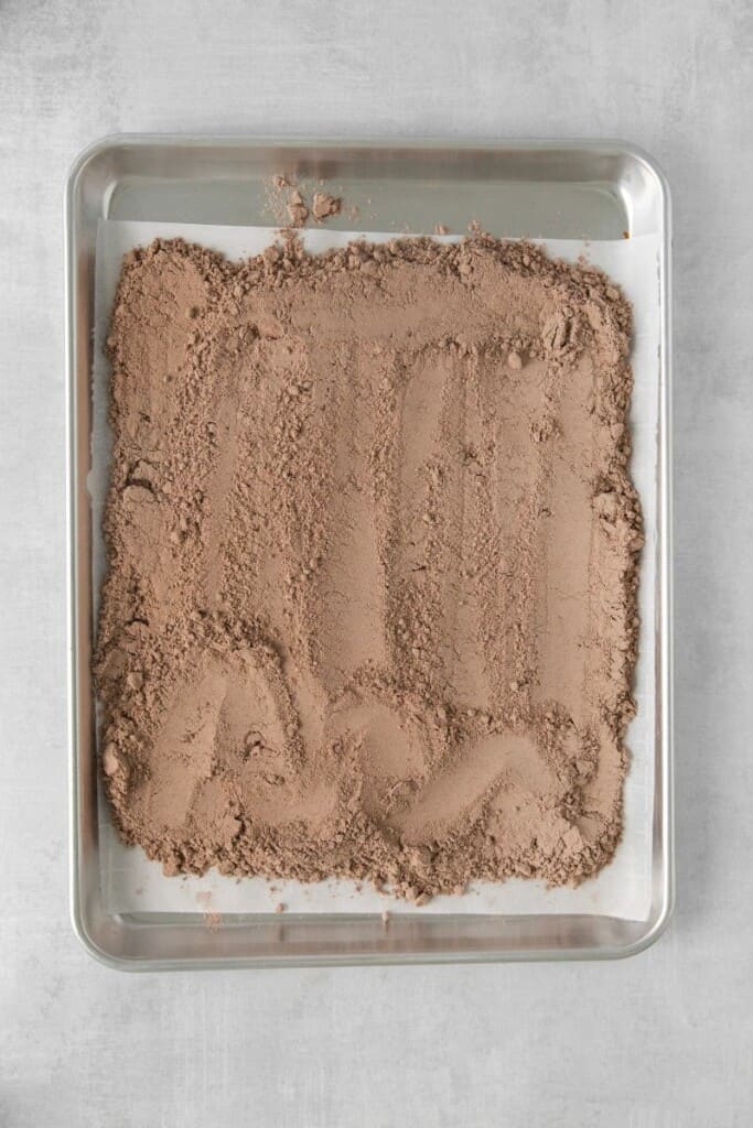 A mistura de brownie espalhada no fundo de uma assadeira forrada com papel manteiga.