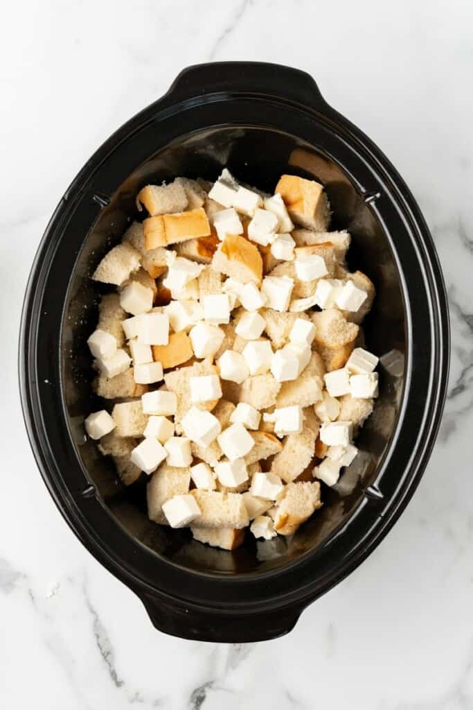 Visão aérea de cubos de pão e cream cheese em uma panela elétrica.