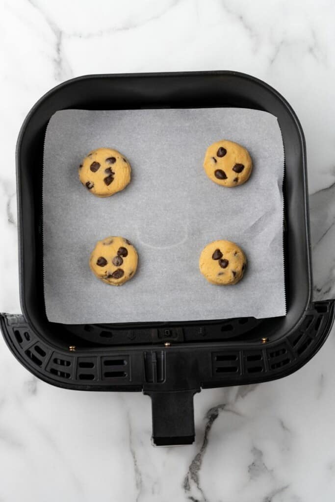 Visão aérea de quatro colheres de massa de biscoito em uma cesta de fritadeira preta forrada com papel manteiga.