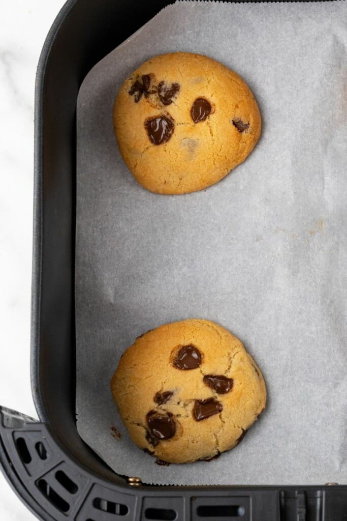 Close-up vista de 2 biscoitos em papel manteiga descansando em uma cesta de fritadeira de ar preto.