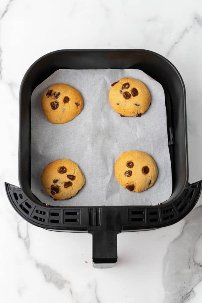 Visão aérea de quatro biscoitos assados ​​em uma fritadeira, sobre papel manteiga em uma cesta preta da fritadeira.
