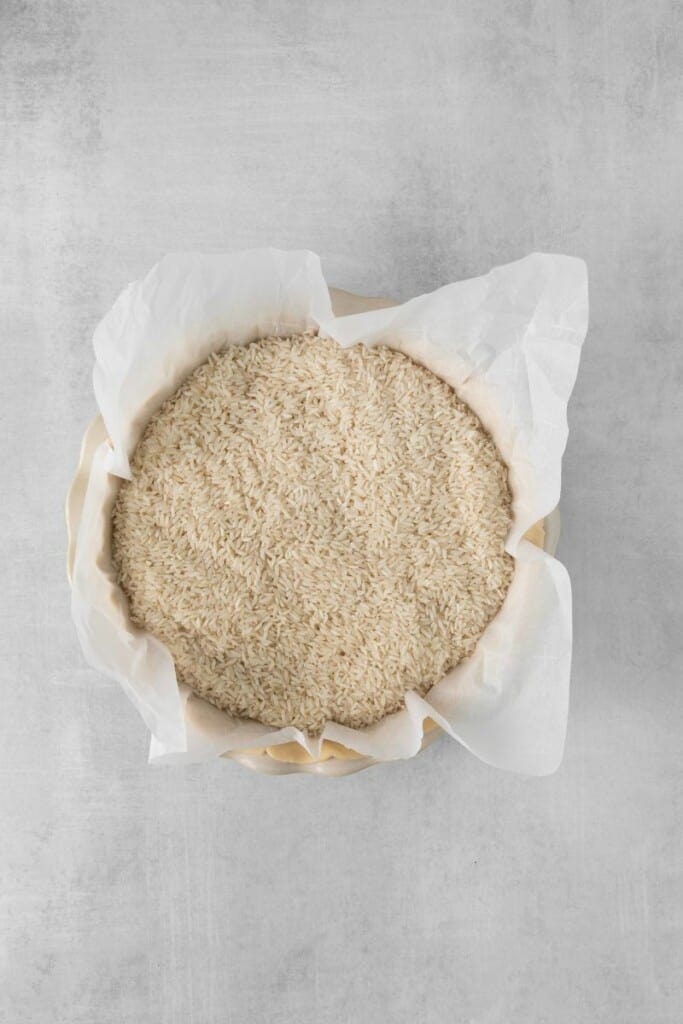 Visão aérea de massa de torta não assada forrada com papel manteiga, recheada com arroz para ser assada.