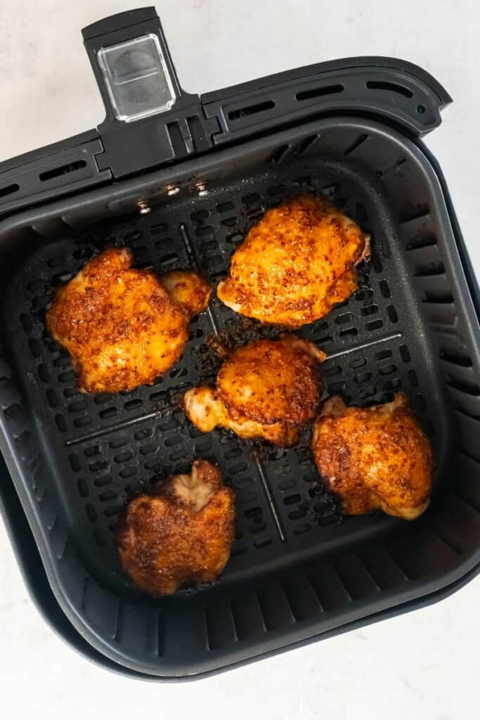 Visão aérea de cinco coxas de frango desossadas fritas ao ar em uma cesta preta de fritadeira.