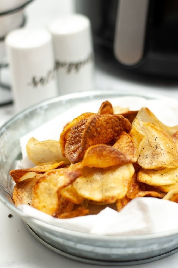 Batatas fritas Air Fryer em uma tigela com sal, pimenta e uma fritadeira ao fundo