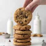 Pilha de biscoitos de chocolate assados ​​com um levantado, garrafas de leite ao fundo.