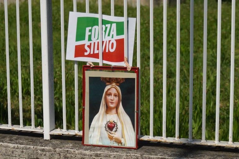 Uma imagem representando a Virgem Maria é colocada ao lado de um logotipo do partido Forza Italia fora do hospital 'San Raffaele', onde o ex-primeiro-ministro italiano Silvio Berlusconi está hospitalizado, em Milão