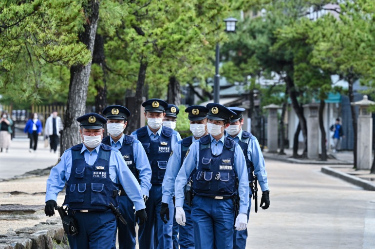 Polícia japonesa em patrulha perto de Hiroshima, Japão, antes da cúpula do G7.  Eles estão caminhando por um caminho arborizado.
