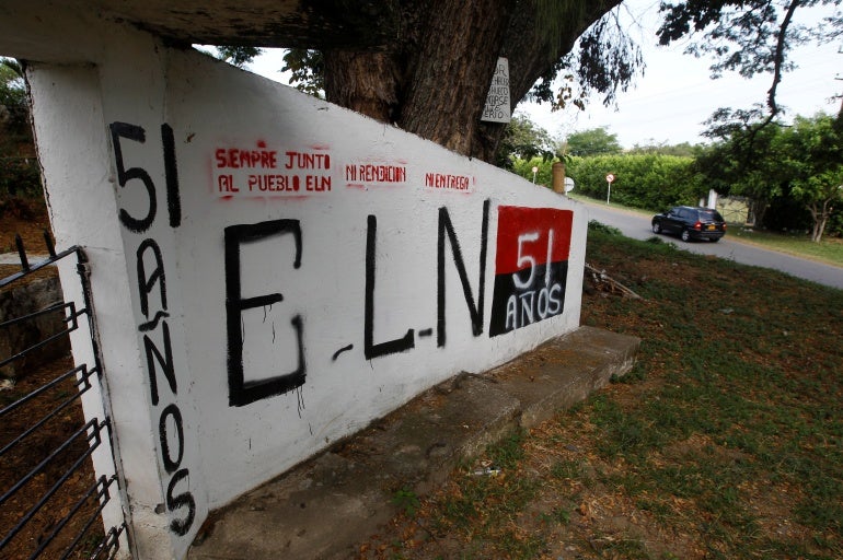 Uma parede branca do lado de fora de um cemitério tem as letras "ELN" e "51 anos" pintado nele.