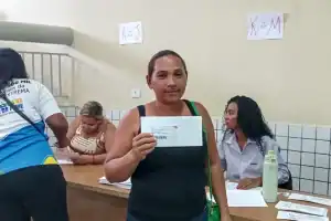 Beneficiária sorridente segurando o cartão do programa social na mão