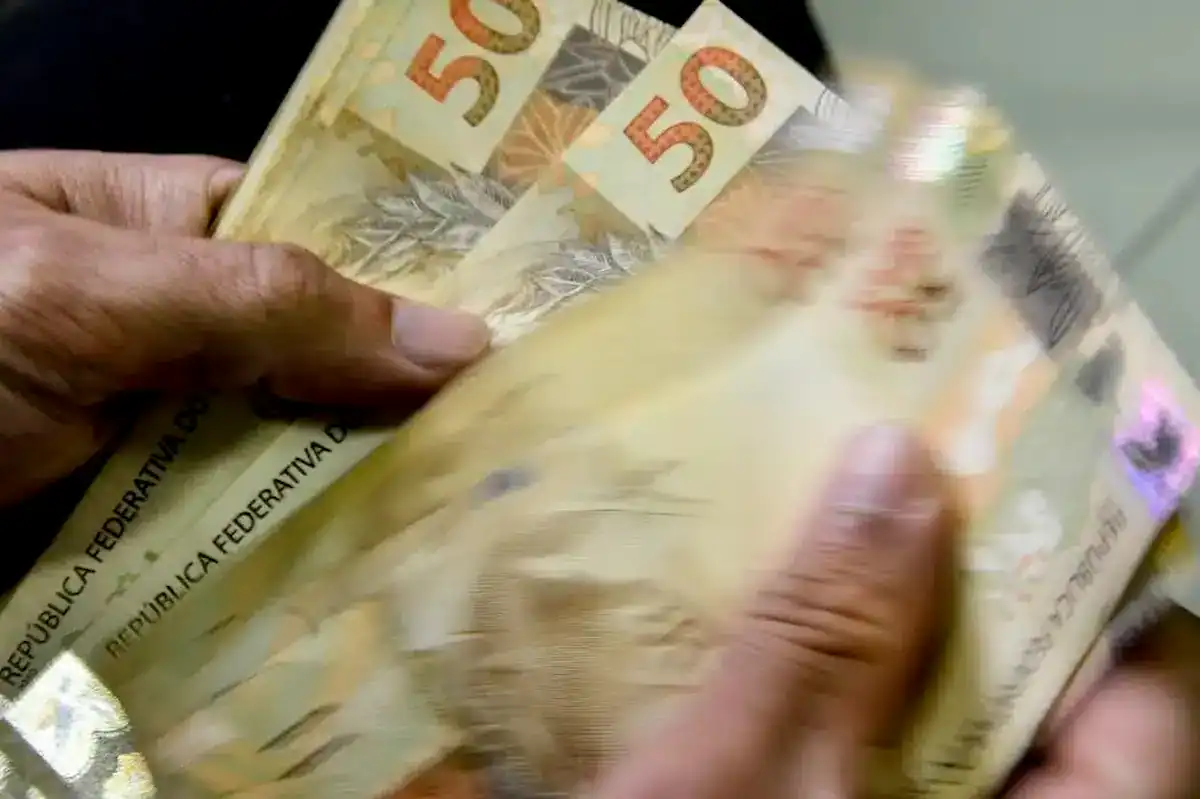 Cédulas de dinheiro e moedas sobre um teclado de computador, com um cadeado digital, simbolizando os valores a receber do Banco Central e os desafios de segurança no acesso online.