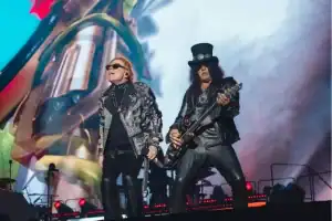 Axl Rose, Slash e Duff McKagan, membros do Guns N' Roses, tocando no palco durante show da turnê mundial.