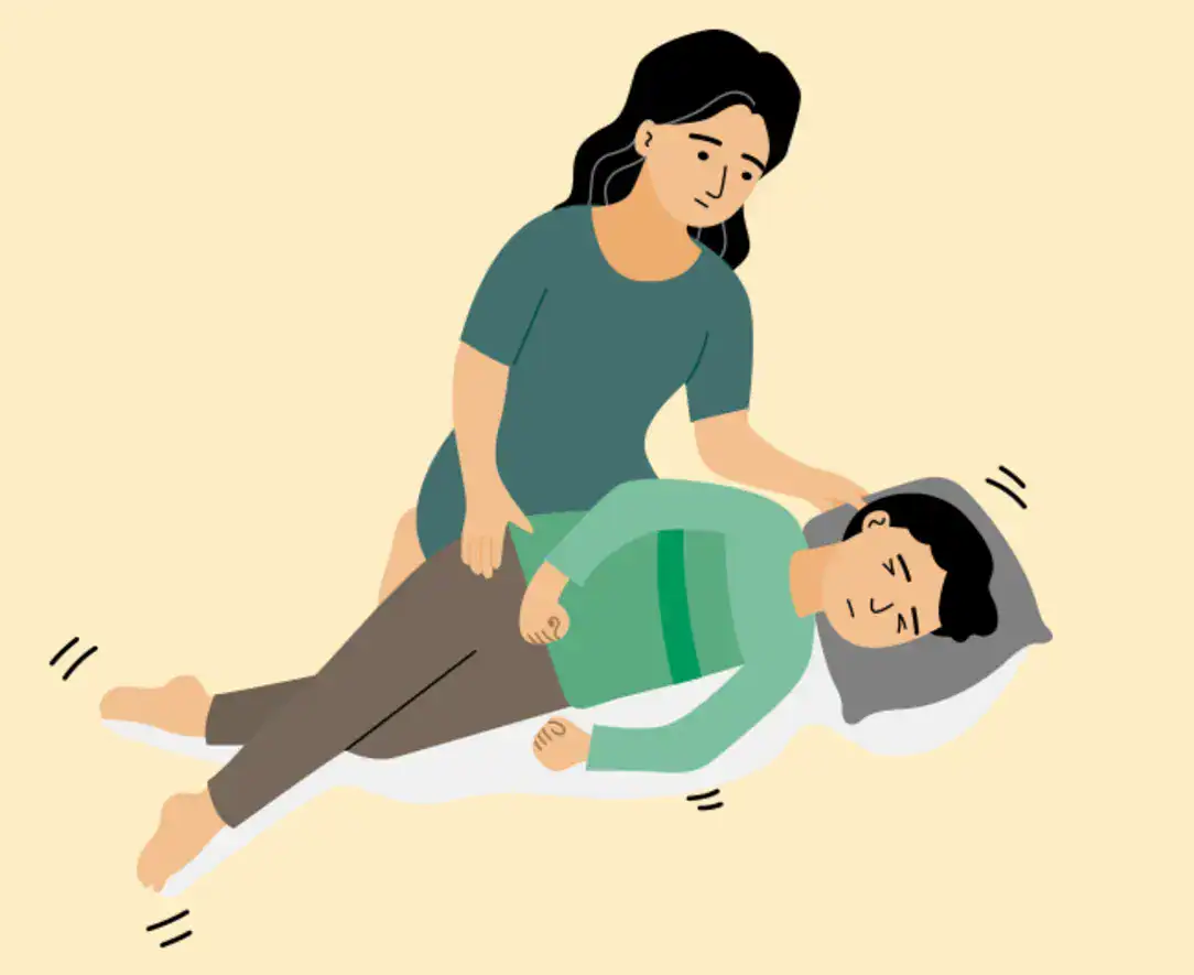 Pessoa ajoelhada prestando primeiros socorros a outra deitada no chão durante uma crise epiléptica, com foco na segurança e apoio.