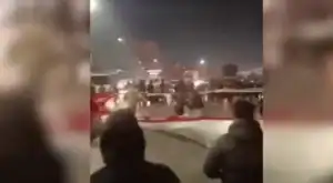 Multidão de manifestantes iranianos em rua, com bandeiras e cartazes, durante protestos contra o regime.