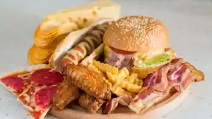 Ilustração de alimentos processados com rótulos de ingredientes e símbolos de alerta, representando a ligação entre conservantes e risco de câncer.