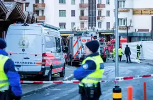 Equipes de resgate e bombeiros no local do incêndio em bar de estação de esqui em Crans-Montana, Suíça, com fumaça e danos visíveis.