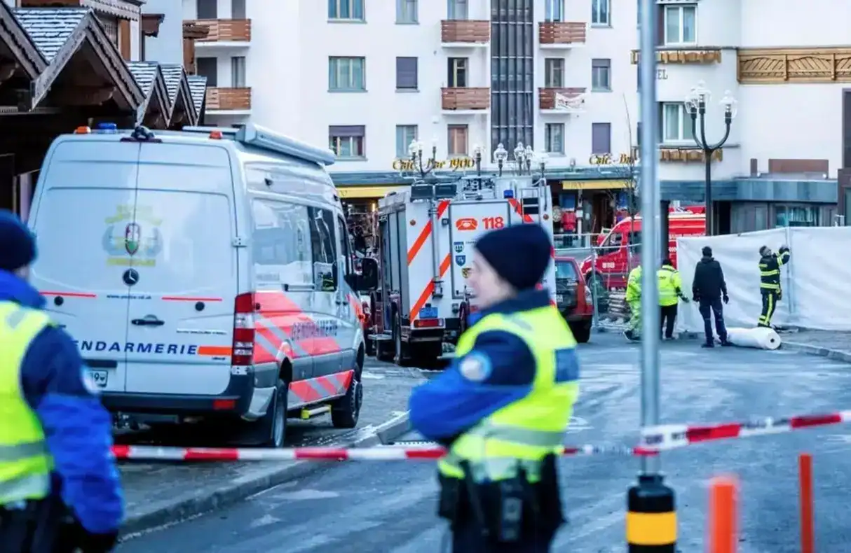 Equipes de resgate e bombeiros no local do incêndio em bar de estação de esqui em Crans-Montana, Suíça, com fumaça e danos visíveis.