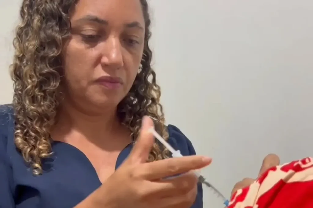 Profissional da saúde com máscara aplica vacina no braço de uma criança em uma unidade de saúde.